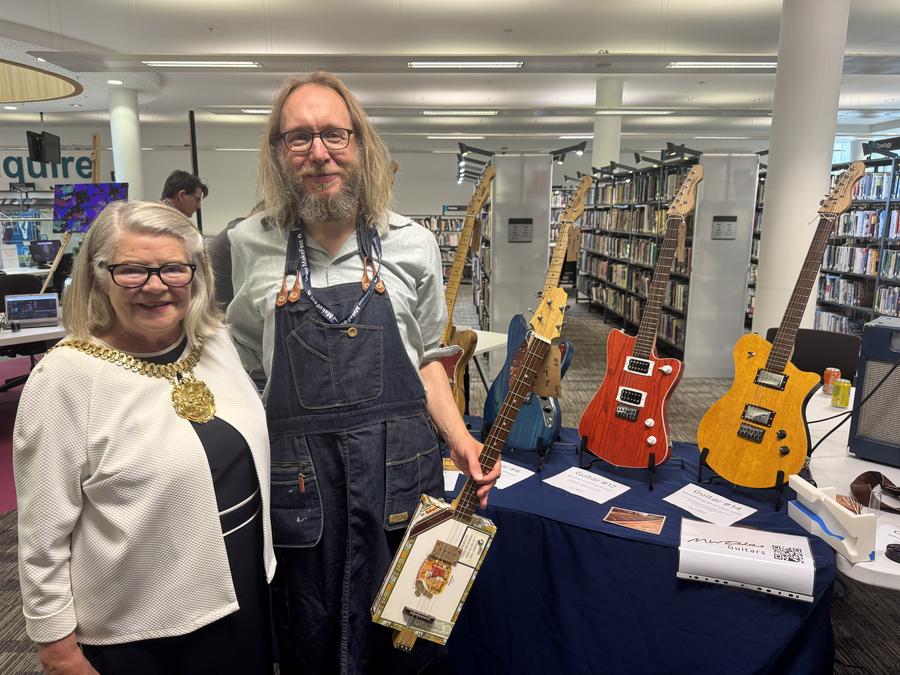A photo of me and the Lord Mayor of Liverpool, wearing a large gold neck piece that is the badge of office, stood in front of a table of guitars, which in turn are in front of shelves of books.