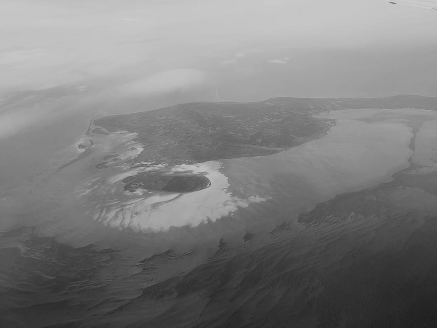 A photo of an island in a sea taken from the window of an airplane. The island has a swirly shape, which is emphasised by the sand banks around it.