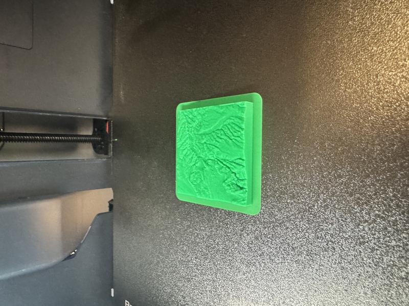 A photo of a small 3D-print, about 5cm per side, of some hilly landscape with what looks like rivers 